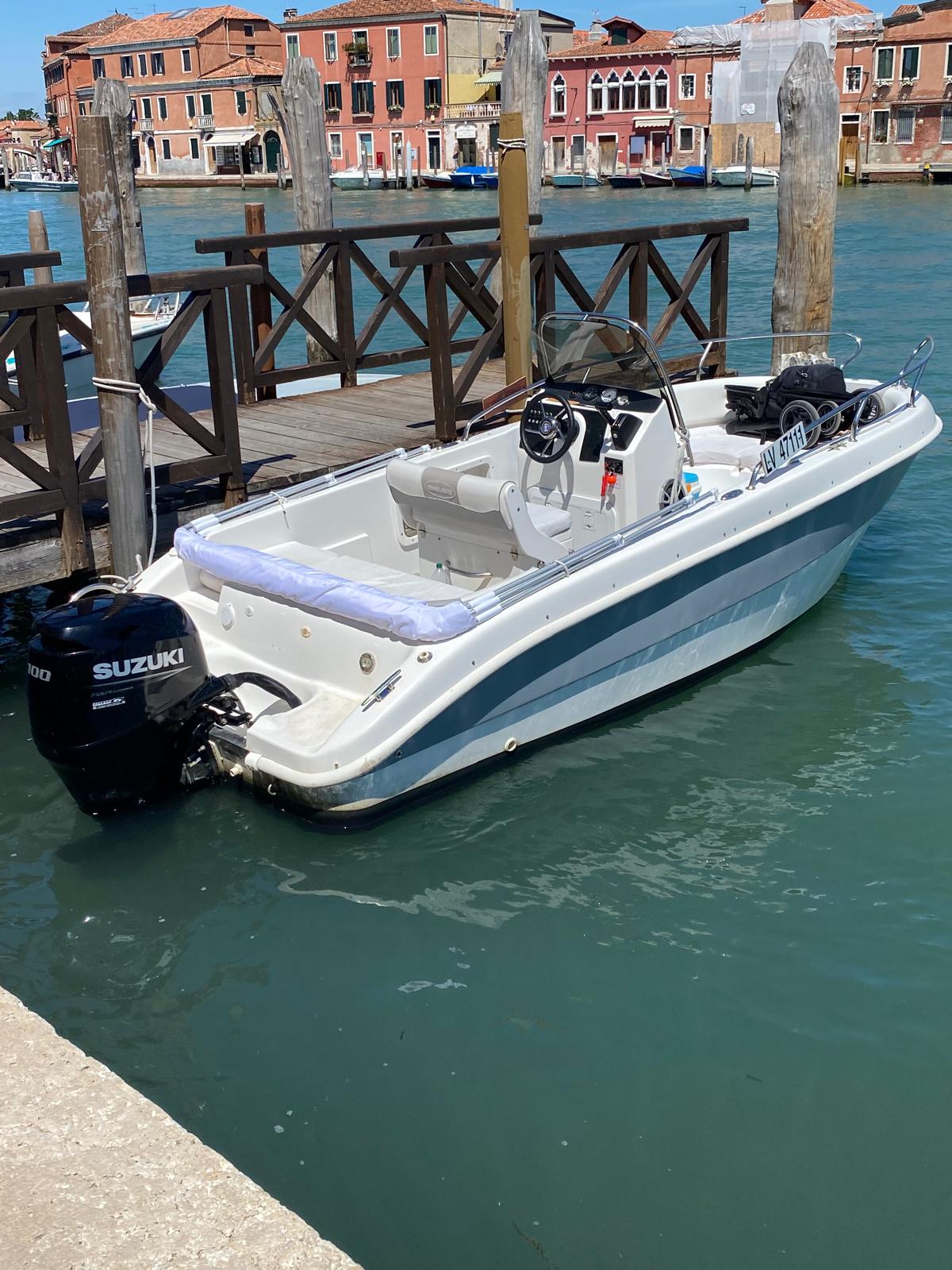 White Venetian Boat with a blue stripe, outboard motor and central helm, moored beside a wooden landing