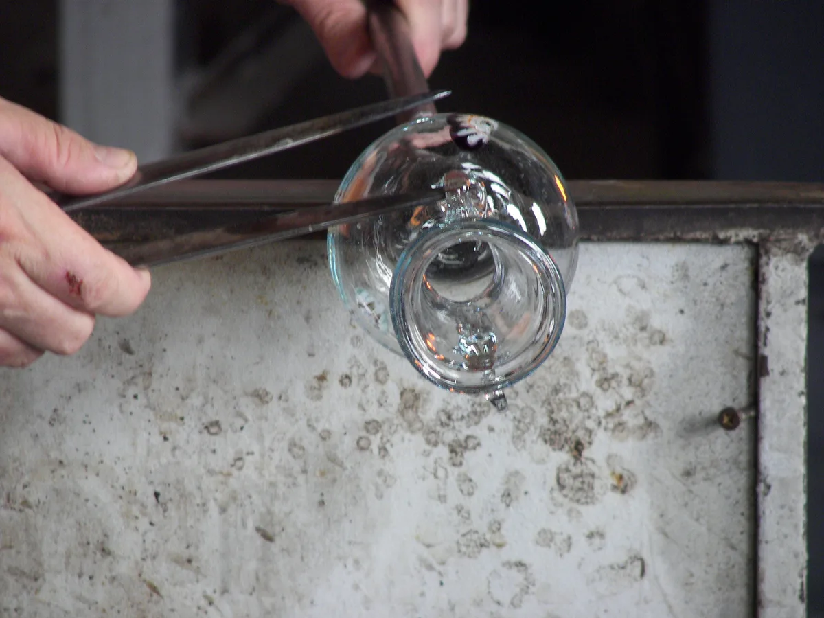 Hands and tools shaping a glass vessel in Murano; illustrative photograph