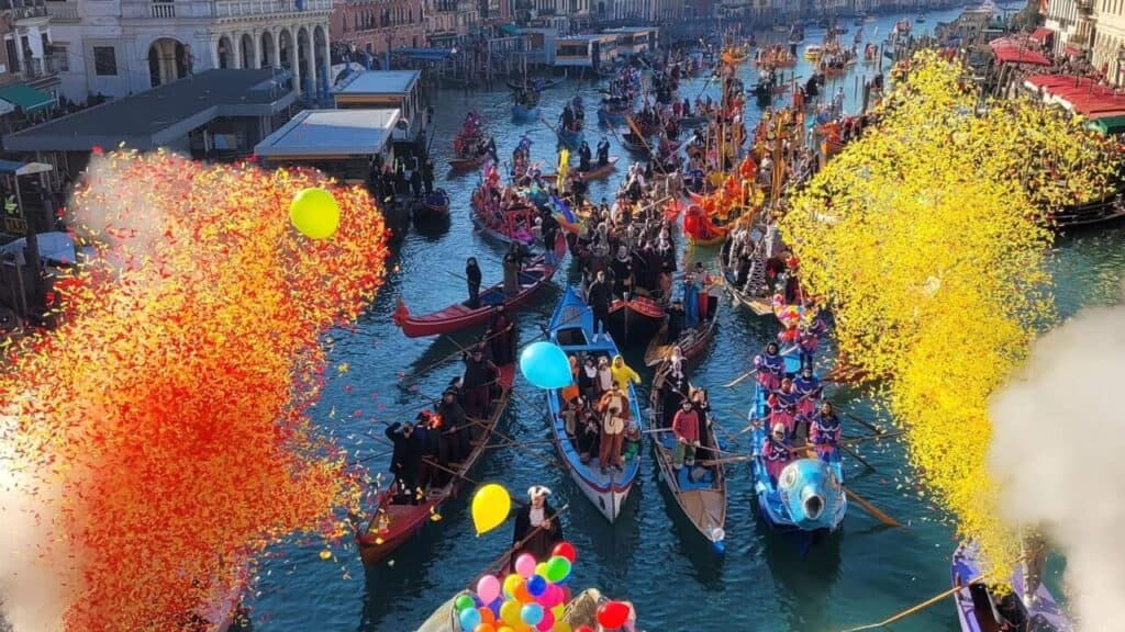 Corteo di barche a remi durante il Carnevale di Venezia, tra palloncini e nuvole di coriandoli gialli e rossi